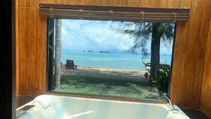 Un baño con una bañera grande, vista a una playa y paredes de madera.