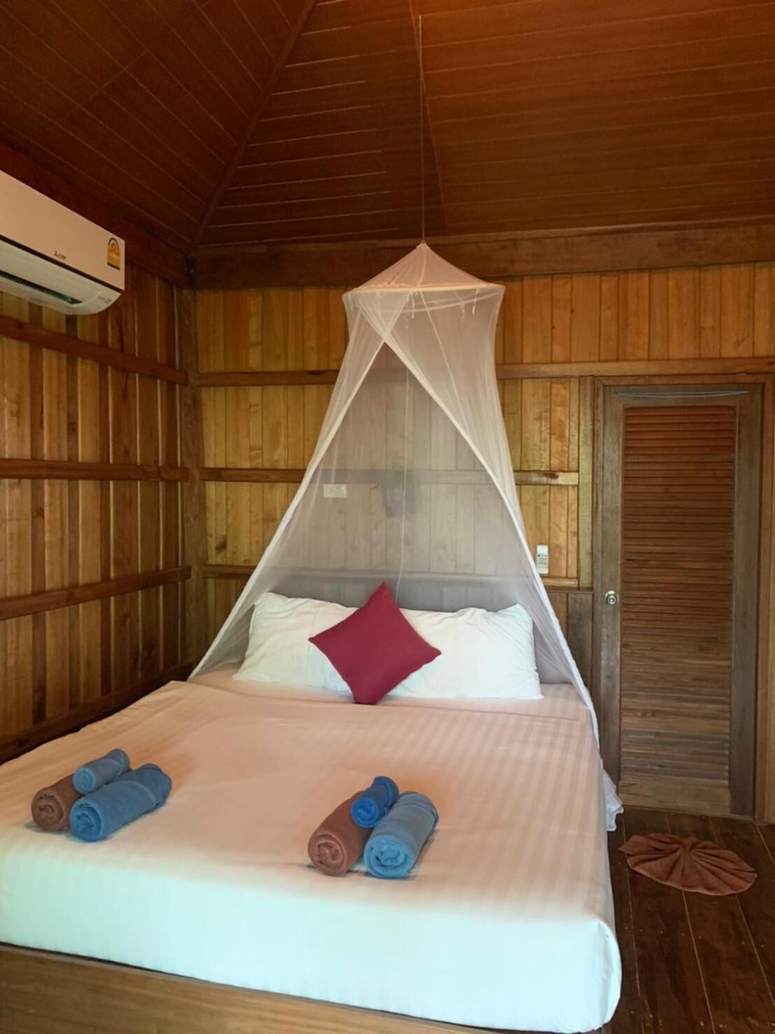 Une pièce en bois avec un lit, une moustiquaire et une porte.