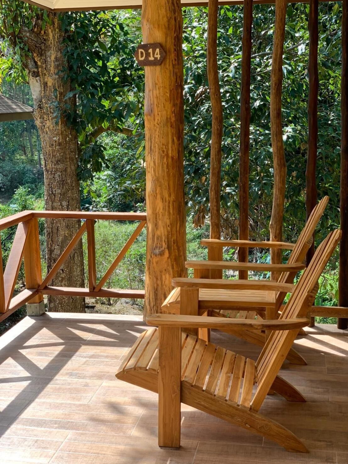 A wooden deck with a wooden chair and a railing, surrounded by trees.