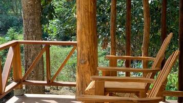 A wooden deck with a wooden chair and a railing, surrounded by trees.