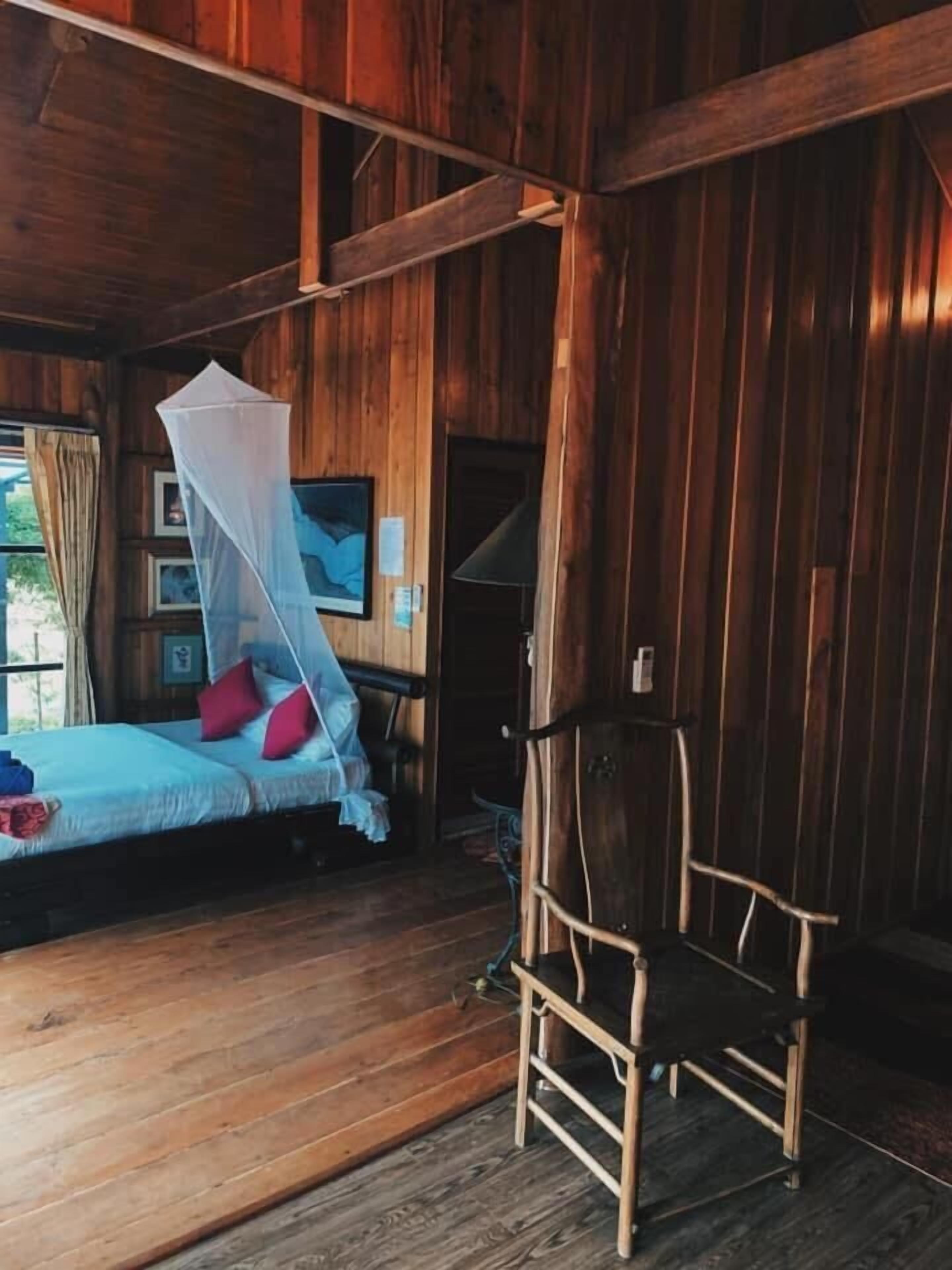 Una habitación de cabaña de madera con una cama, una silla y un mosquitero.