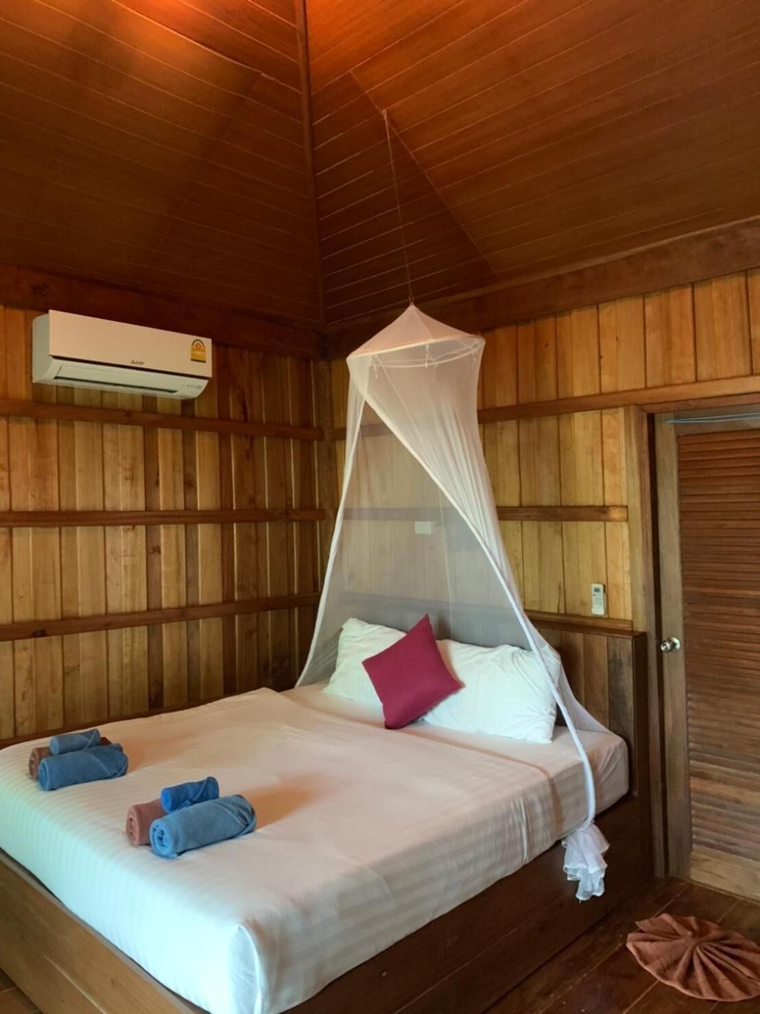 Una habitación de madera con una cama, mosquitero y aire acondicionado.
