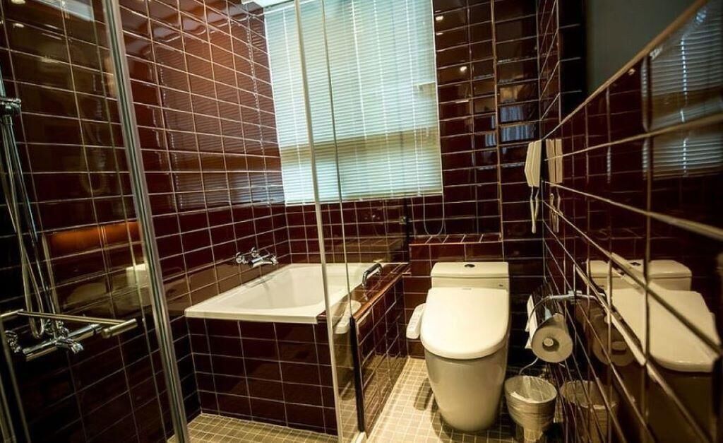 A bathroom with a glass-enclosed shower, a bathtub, a toilet, and a window with blinds.