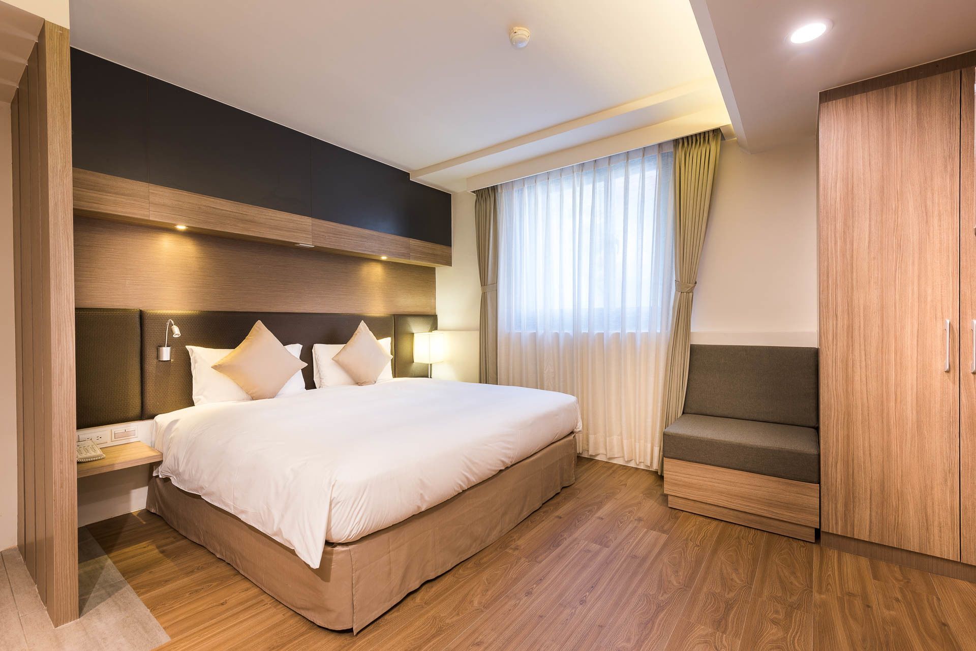 A modern hotel room with a large bed, bedside lamps, a sofa, and a wardrobe.