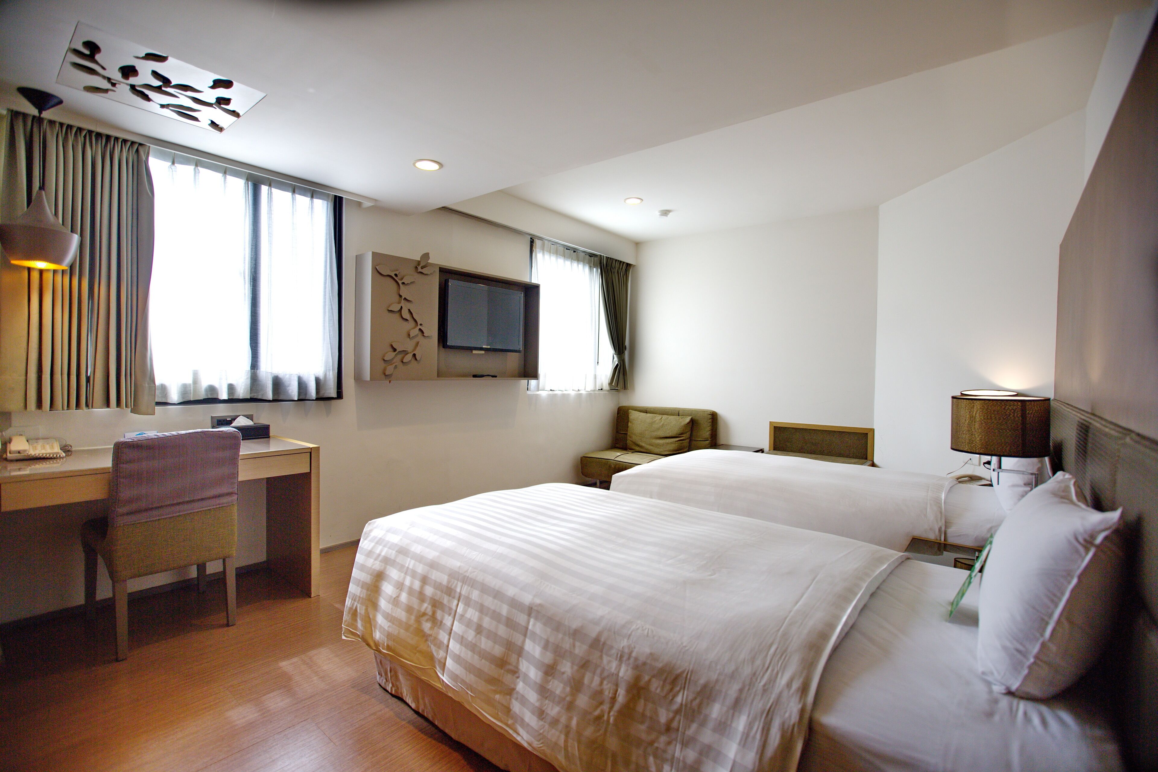 A hotel room with two beds, a desk, a chair, a television, and a lamp.