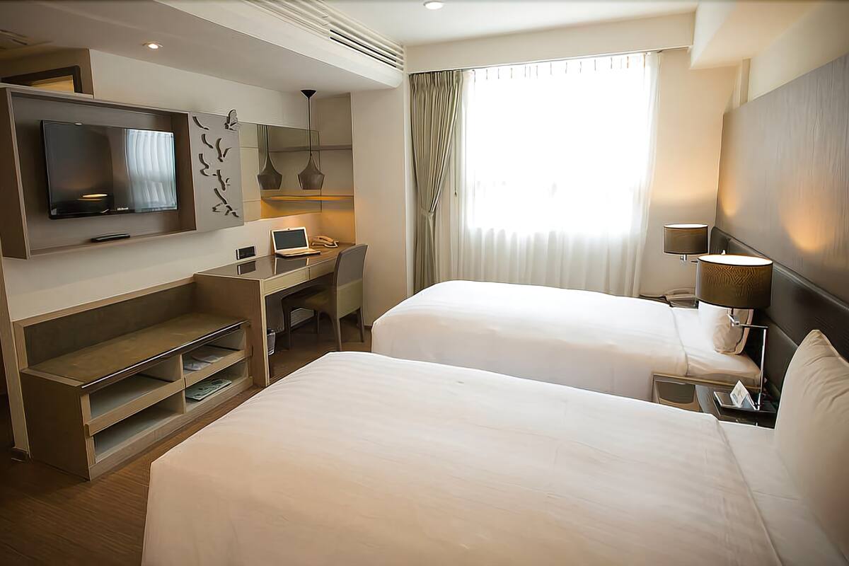 Une chambre d’hôtel avec deux lits, une télévision, un bureau et une fenêtre avec des rideaux.