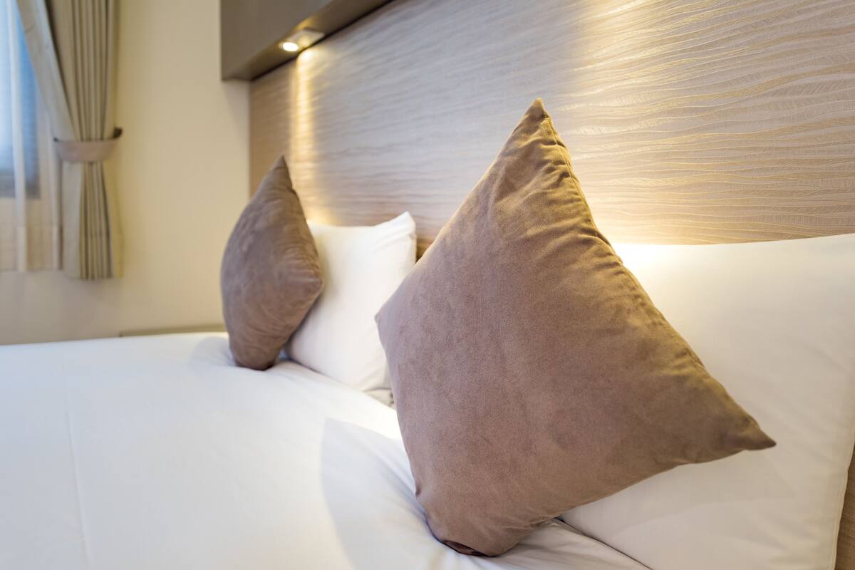 Un lit bien fait, avec du linge de lit blanc et deux oreillers beige.