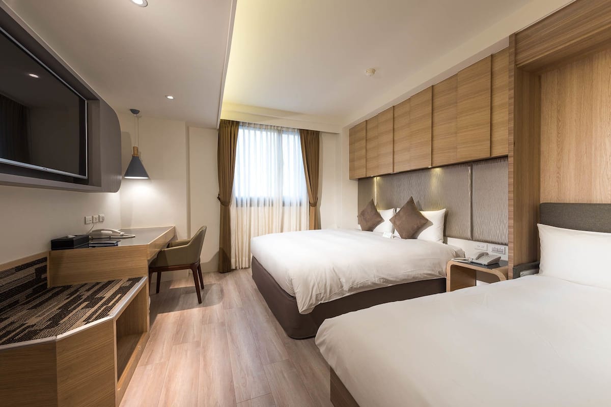 Une chambre d’hôtel avec un grand lit, un bureau avec une chaise, une télévision et une fenêtre avec des rideaux.