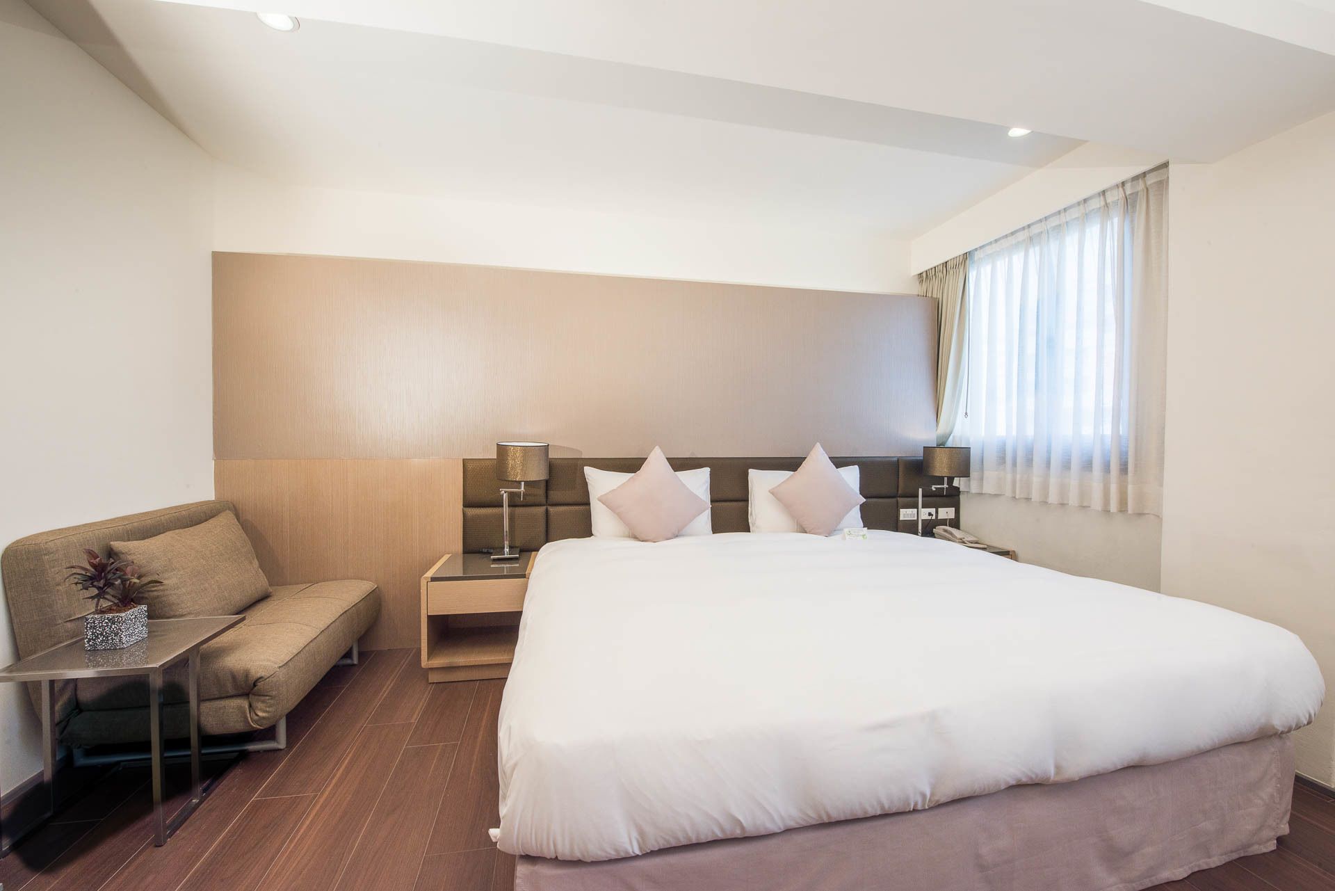 Une chambre d’hôtel moderne avec un grand lit, un canapé, une table de chevet et une lampe.