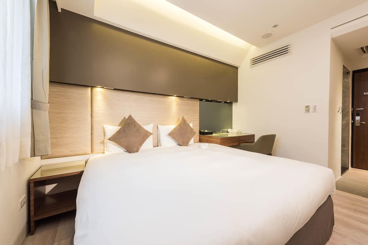 Une chambre d’hôtel moderne avec un grand lit, un bureau avec une chaise et un grand miroir.