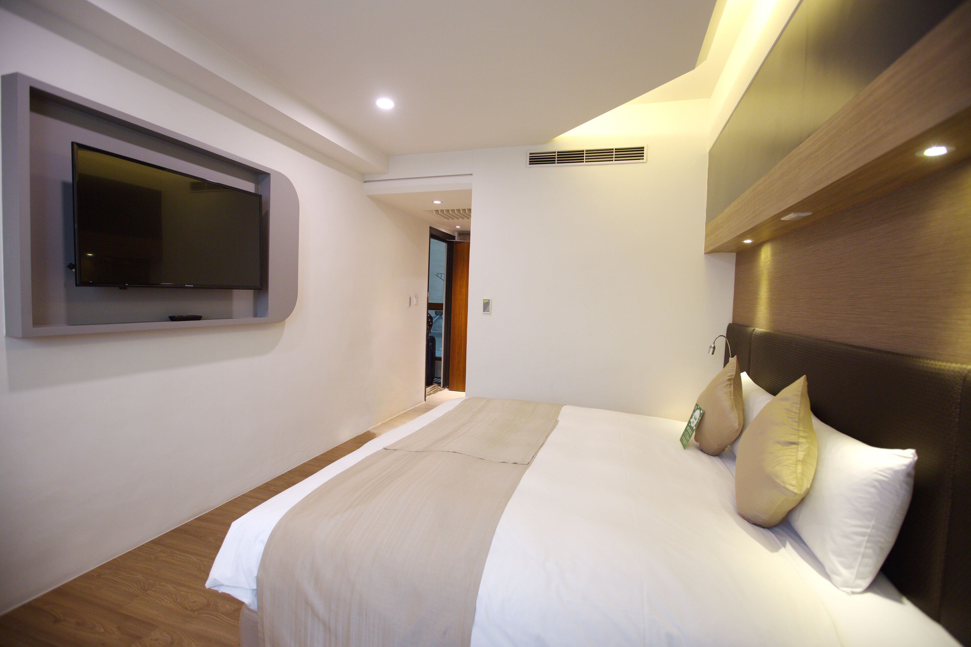 Una habitación de hotel moderna con una cama grande, un televisor de pantalla plana montado en la pared y un cabecero de madera.
