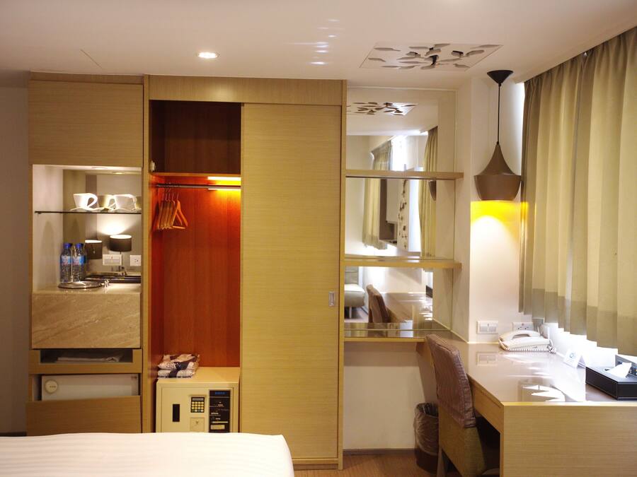 A hotel room with a bed, a desk with a lamp, a wardrobe, and a mirror.