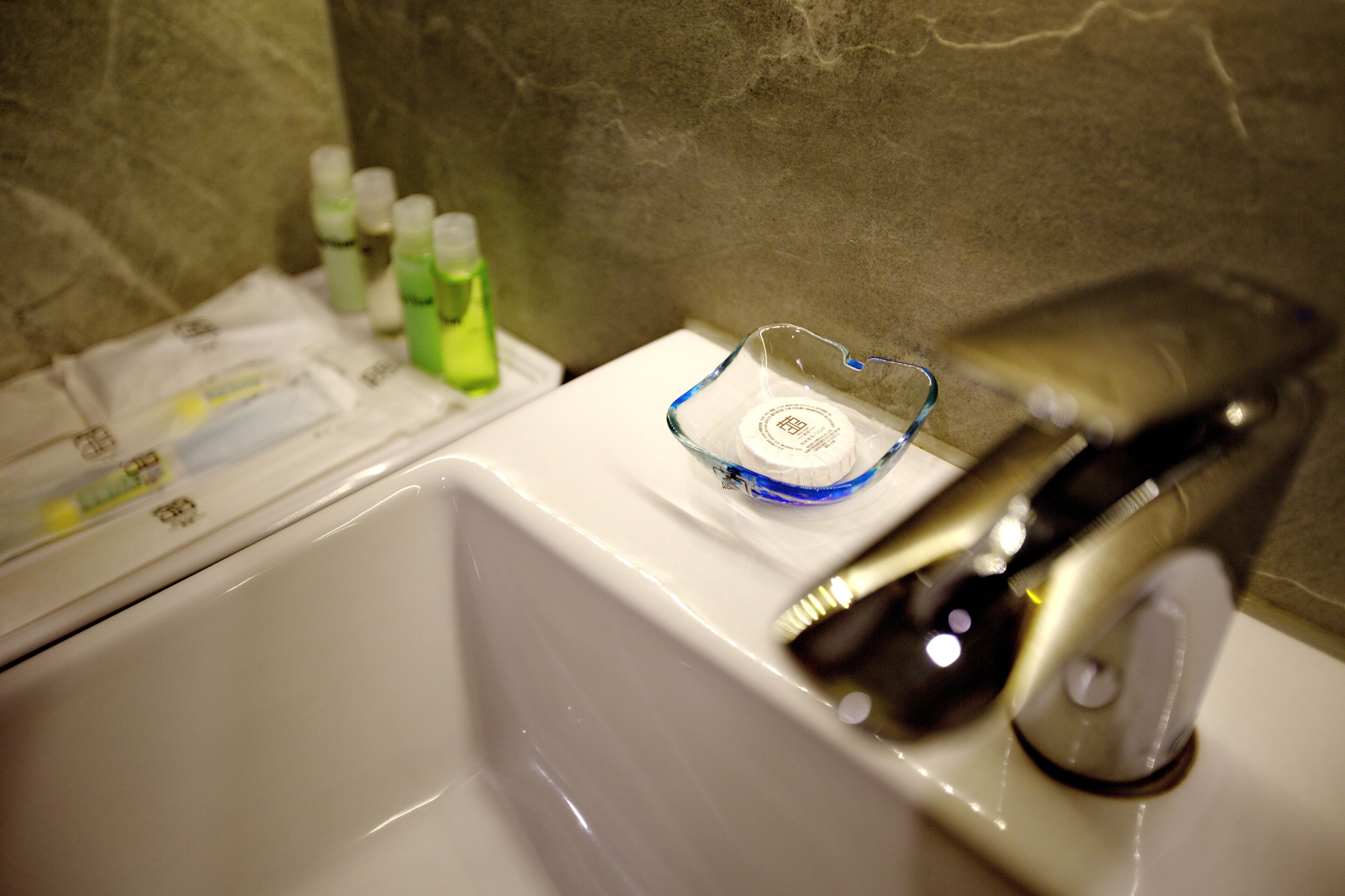 Un lavamanos de baño con un jabonero de vidrio, un grifo y varias botellas de jabón.