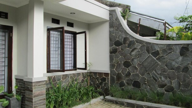 Una casa moderna con un muro de piedra, un porche cubierto y plantas en macetas.
