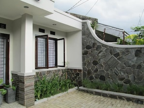Una casa moderna con un muro de piedra, un porche cubierto y plantas en macetas.