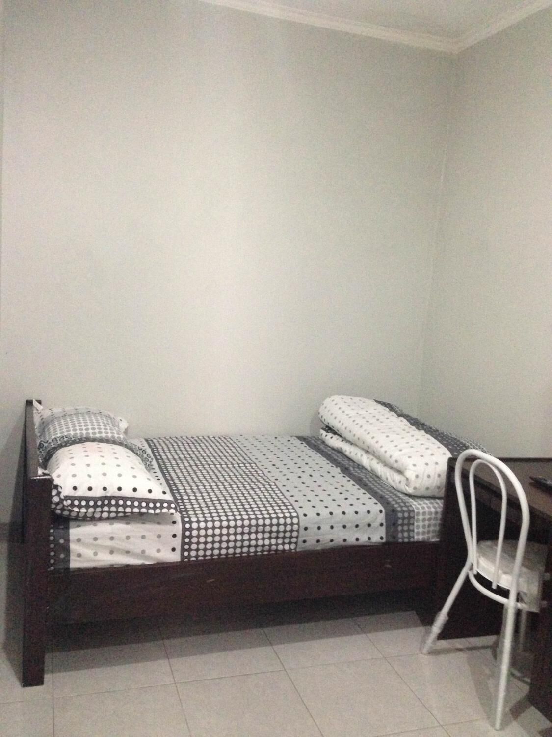 Een kleine kamer met een enkel bed, houten frame, witte wanden en een betegelde vloer.
