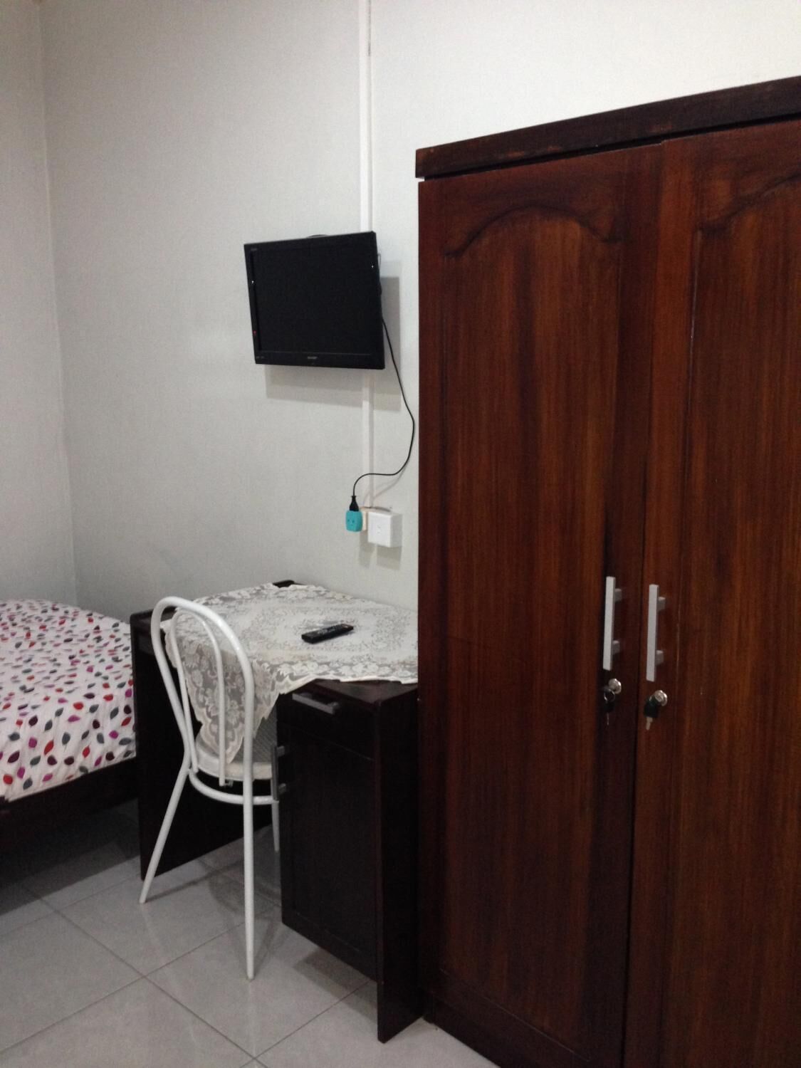 Un dormitorio con cama, escritorio, silla, armario y televisor montado en la pared.