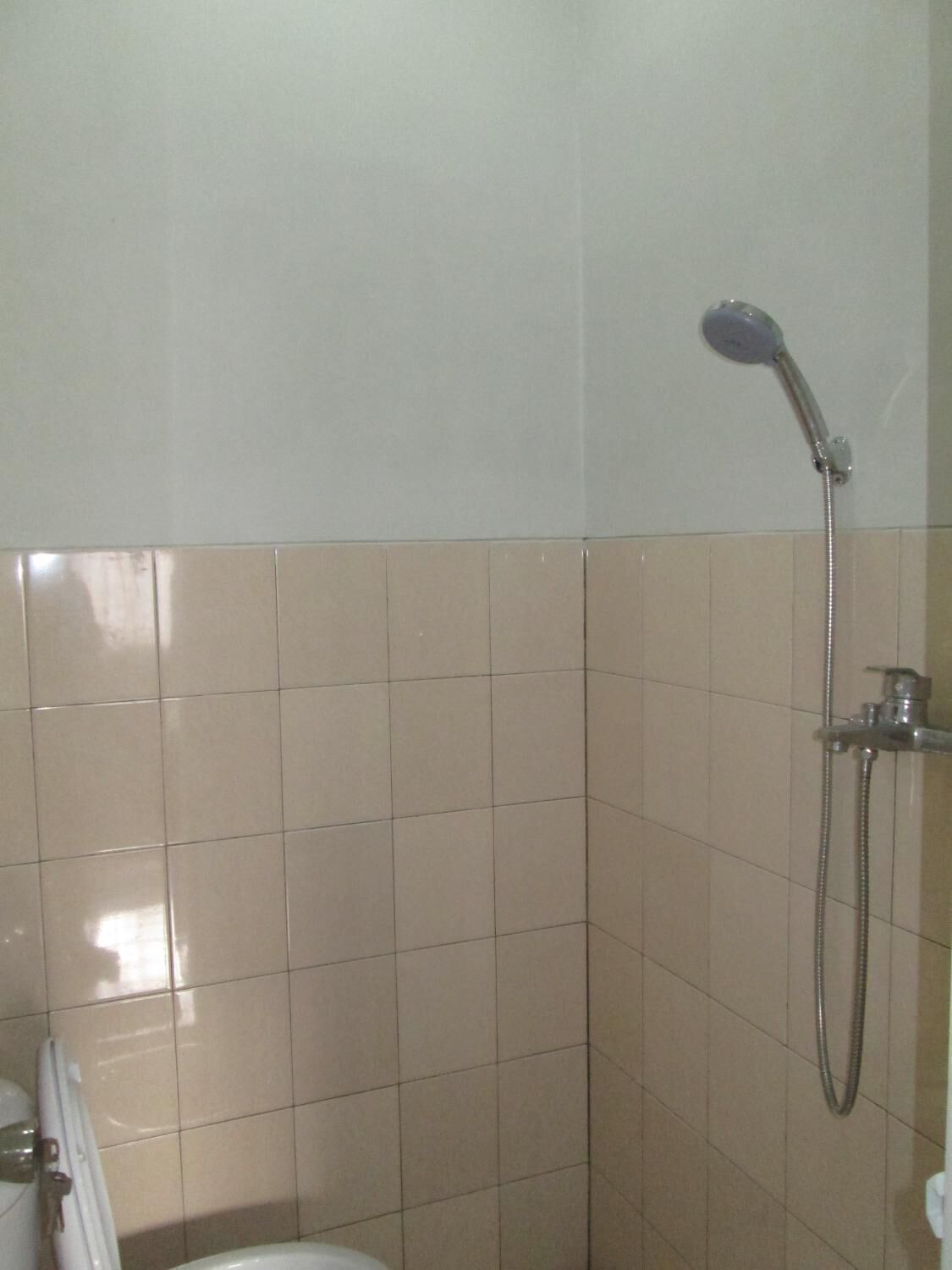 A bathroom with beige tiles, a shower with a handheld showerhead, and a toilet.