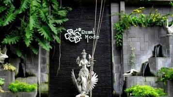 A statue in front of a black wall with the text "Rumah Mode" and a logo.