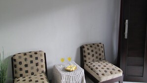 Una habitación con dos sillones estampados, una pequeña mesa con bebidas y un plato, y una puerta.