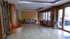 Un hall d’entrée spacieux avec un sol en marbre, un coin salon doté de canapés et de grandes fenêtres offrant une vue sur l’extérieur.