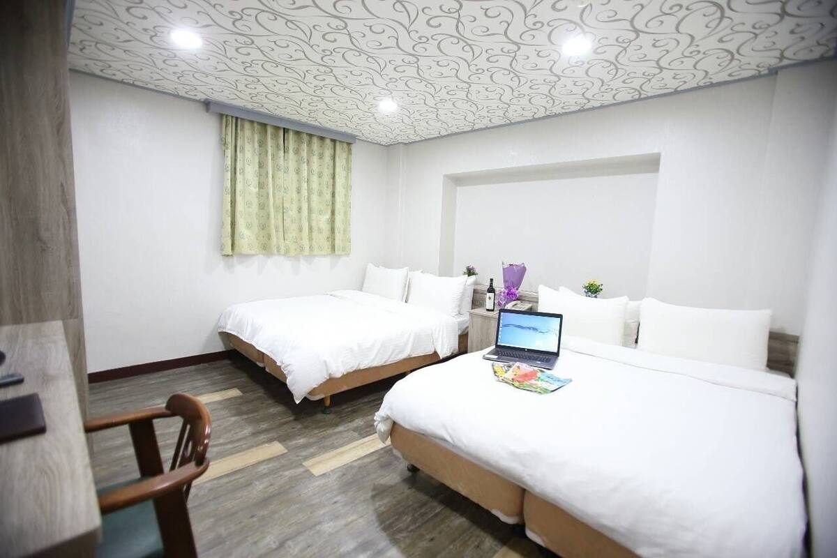 A hotel room with two beds, a desk, and a laptop.