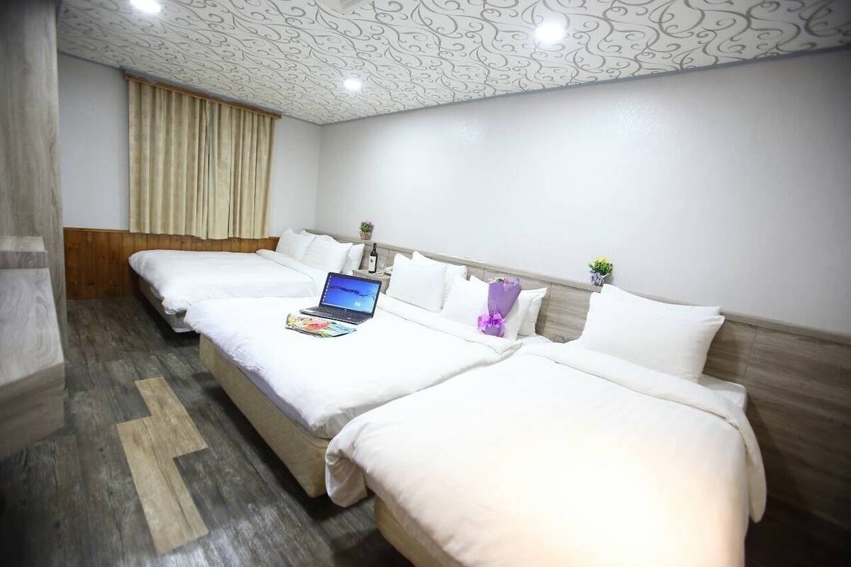 A hotel room with three beds, a laptop on the middle bed, and a window with curtains.