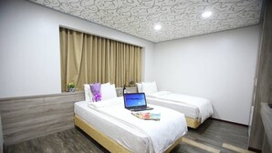 Une chambre d’hôtel avec deux lits, un ordinateur portable posé sur l’un des lits et une fenêtre avec des rideaux.