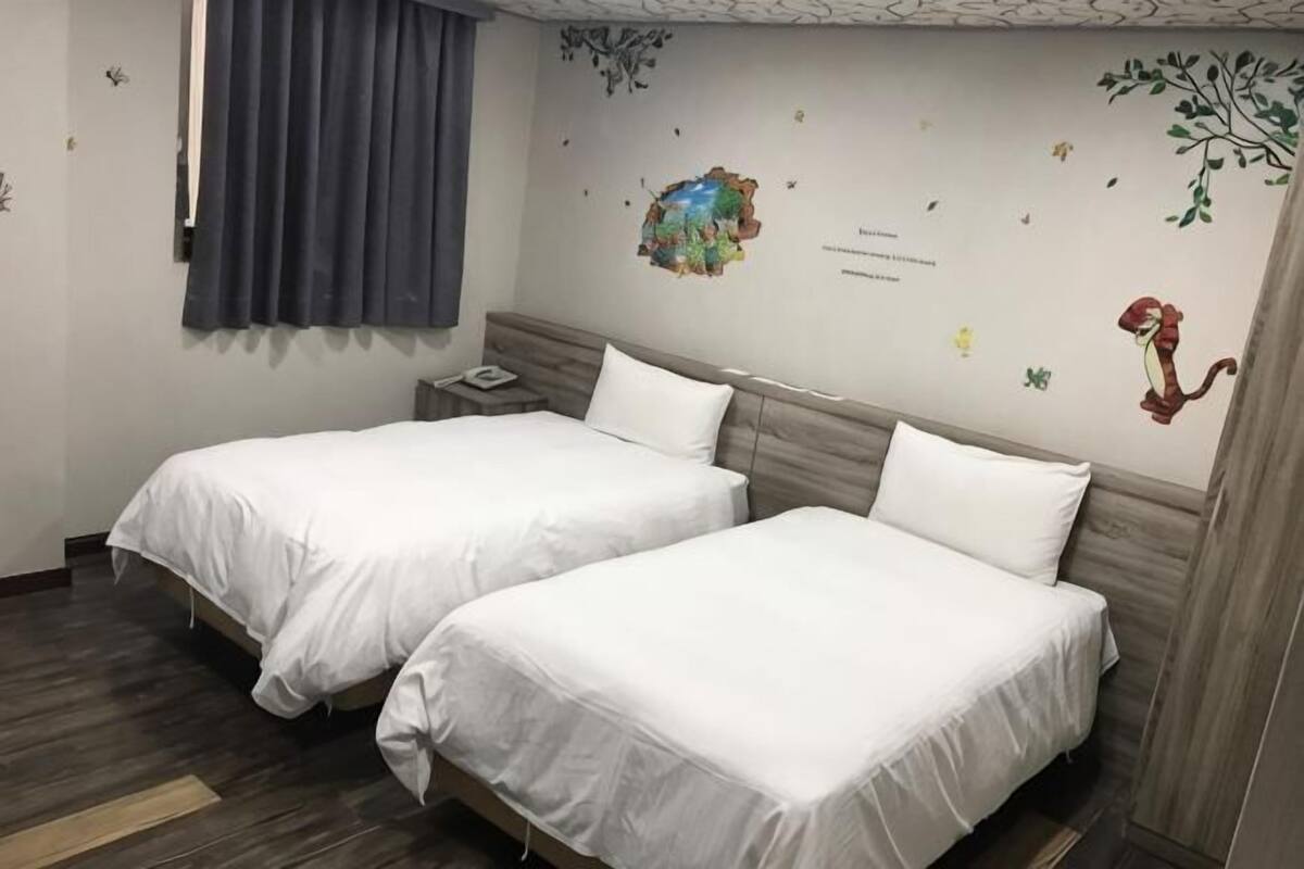 A hotel room with two beds, a nightstand, a wall clock, and a window with curtains.