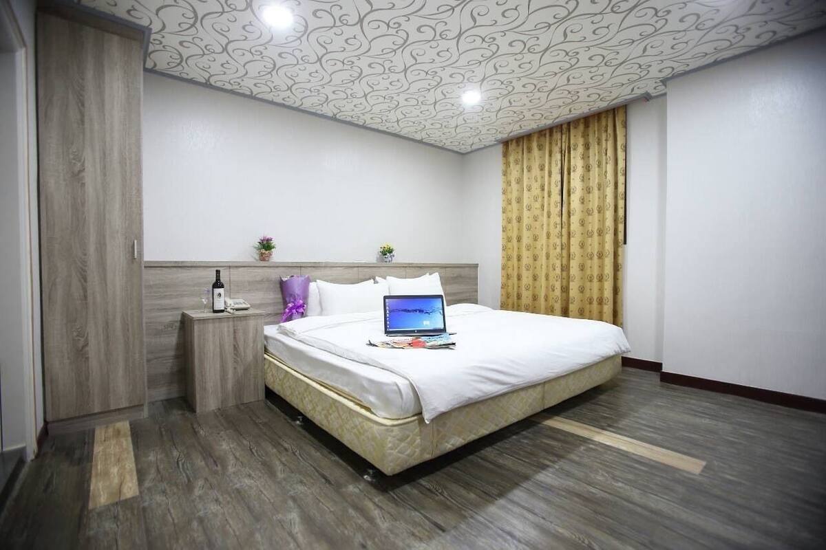 A hotel room with a large bed, a bedside table with a lamp, a laptop, and a small potted plant.