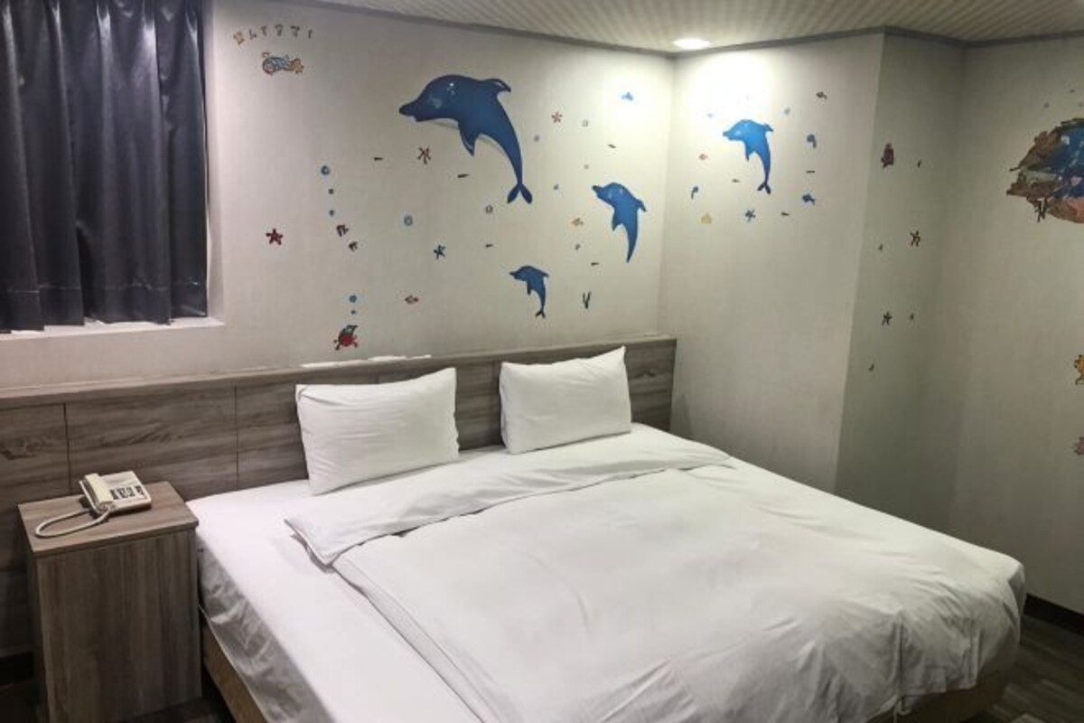 A hotel room with a bed, a nightstand with a phone, and wall decals of dolphins and stars.