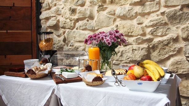 A breakfast setup with bread, fruits, and a vase of flowers against a stone wall. - Moinhos da Gozundeira - Casa no Campo (Sobral de Monte Agraco)