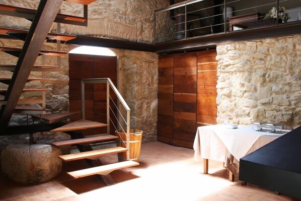A rustic interior with a stone wall, wooden staircase, and a dining area with a table and benches.