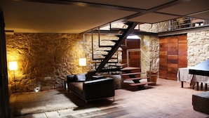 A cozy room with a stone wall, a staircase, a leather sofa, and a table with a lamp. - Moinhos da Gozundeira - Casa no Campo (Sobral de Monte Agraco)