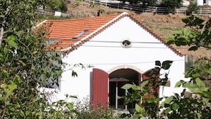 A white building with a red-tiled roof and a red door, surrounded by greenery. - Moinhos da Gozundeira - Casa no Campo (Sobral de Monte Agraco)