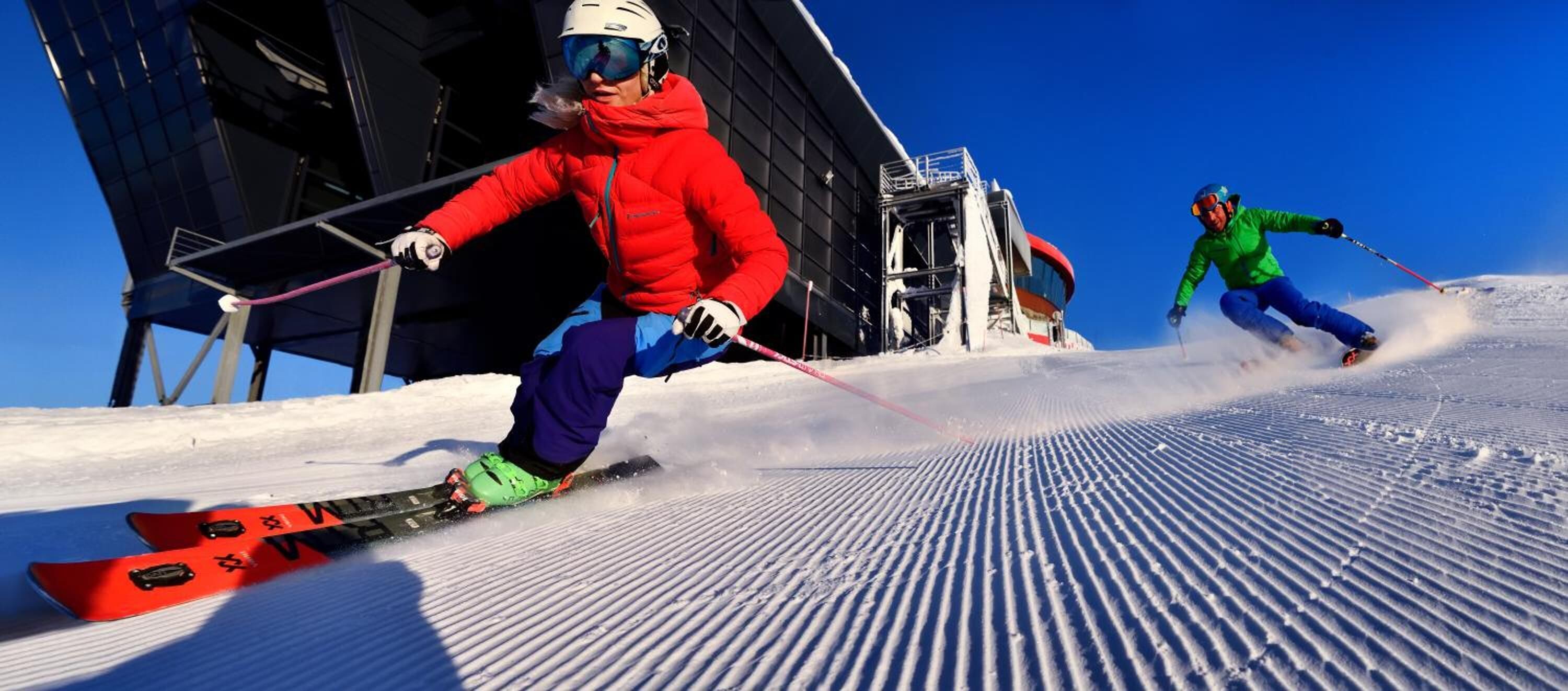 Une piste de ski avec des skieurs en mouvement, une structure de télésiège et un ciel bleu dégagé.