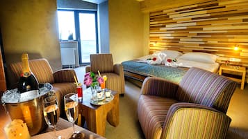 A hotel room with a bed, a sofa, a dining table with drinks, and a view of the outdoors.