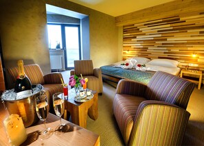 A hotel room with a bed, a sofa, a dining table with drinks, and a view of the outdoors. - Hotel Rotunda (Horna Lehota)