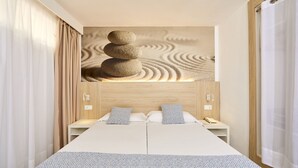 A double bed with a patterned bedspread, two bedside tables with lamps, and a wall-mounted artwork of stacked stones. - Sun Beach (Calvia)