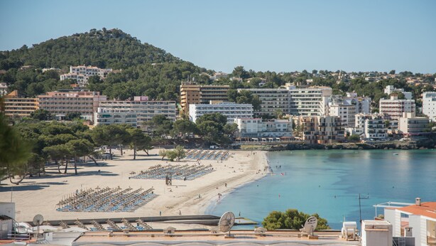 A coastal cityscape with a beach, rows of blue beach chairs, and buildings in the background. - Sun Beach (Calvia)