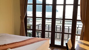 A hotel room with a bed, a wooden desk, and a view of a dock and water. - Phi Phi Green House (Ko Phi Phi)