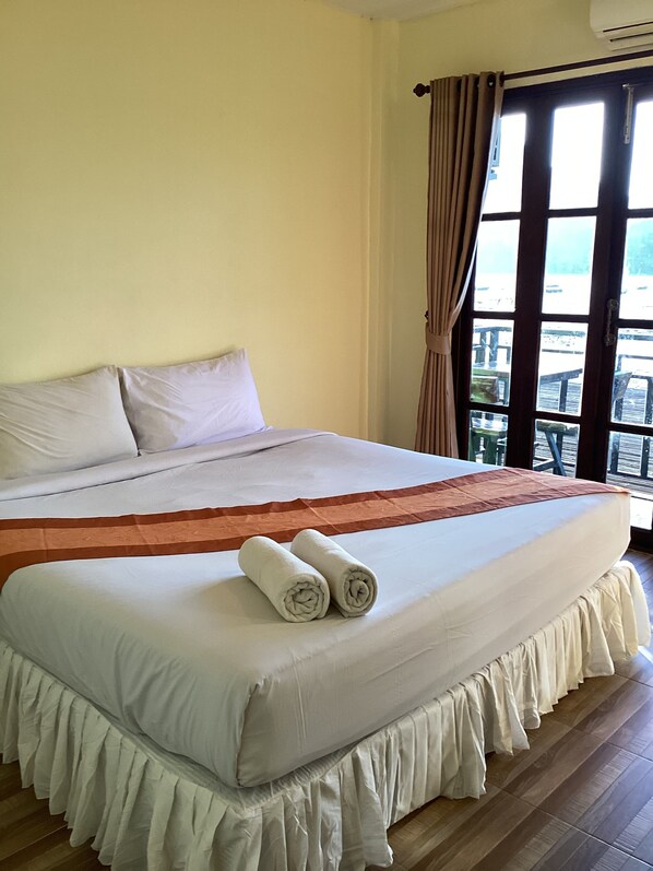 A large bed with white linens, a brown bedspread, and two rolled towels.