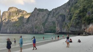 A beach with people walking along the shore, cliffs in the background, and calm water. - Phi Phi Green House (Ko Phi Phi)