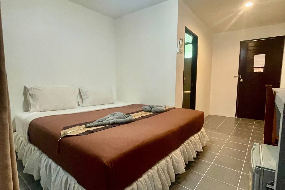 A hotel room with a bed, a small table, a door, and a ceiling light.