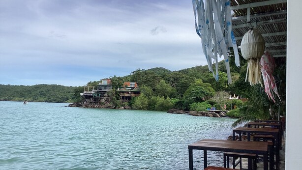 A waterfront restaurant with outdoor seating overlooking a lake, surrounded by lush greenery and a rocky shoreline. - Phi Phi Green House (Ko Phi Phi)