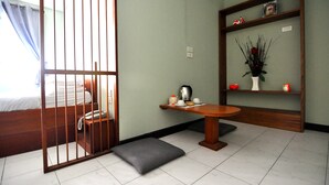 Quarto com cama, mesa com chaleira, vaso com flores e prateleira com objetos decorativos.