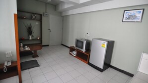 Quarto pequeno e limpo, com televisão, frigorífico e uma prateleira com objetos decorativos.