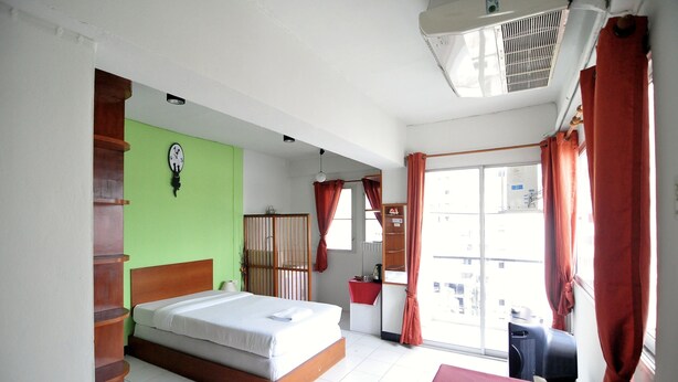 Quarto de hotel com uma cama, janela com cortinas, mesa de cabeceira com caixa de lenços e ar-condicionado fixado na parede.