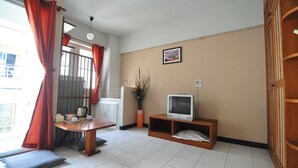 Um espaço de estar compacto com uma mesa de jantar, uma televisão sobre um suporte de madeira, um sofá e uma janela com cortinas vermelhas.