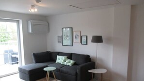 Een moderne woonkamer met een hoekbank, twee bijzettafeltjes, een vloerlamp en een groot raam.